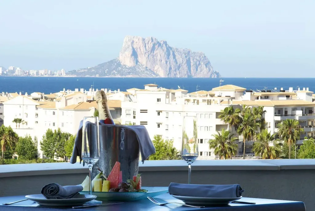 Une table dressée avec des fruits et une bouteille de champagne offre une vue sur la mer et la ville.