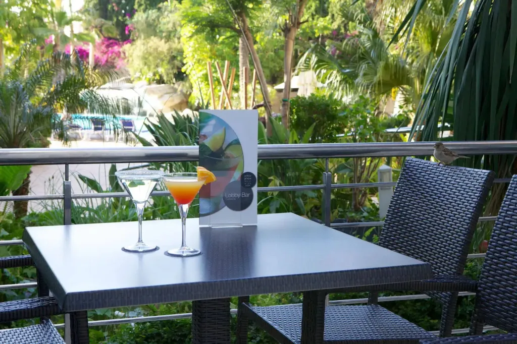 Deux cocktails colorés sont servis sur une table de terrasse avec des chaises en osier.