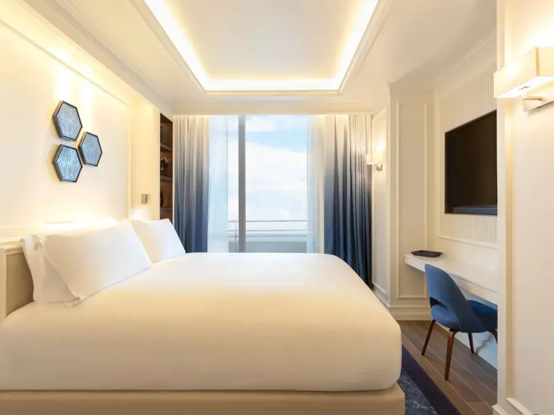 Une chambre lumineuse avec un grand lit et un bureau près d'une fenêtre.