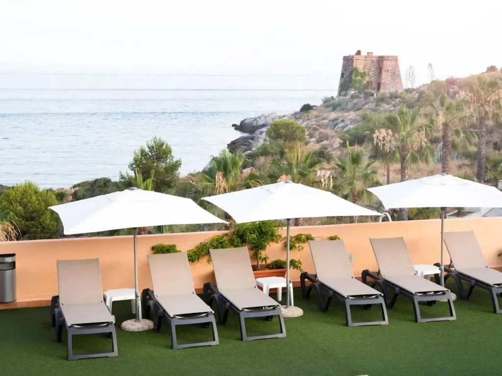 Transats blancs sous des parasols sur une terrasse avec vue sur la mer.
