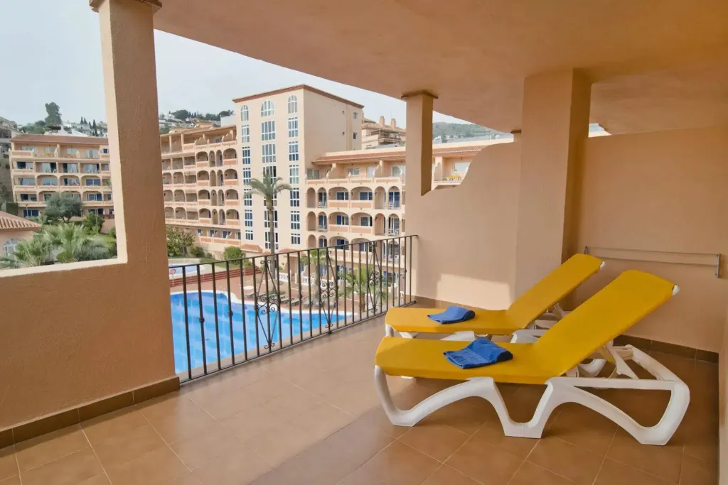 Deux transats jaunes sur une terrasse avec vue sur une piscine et des bâtiments.