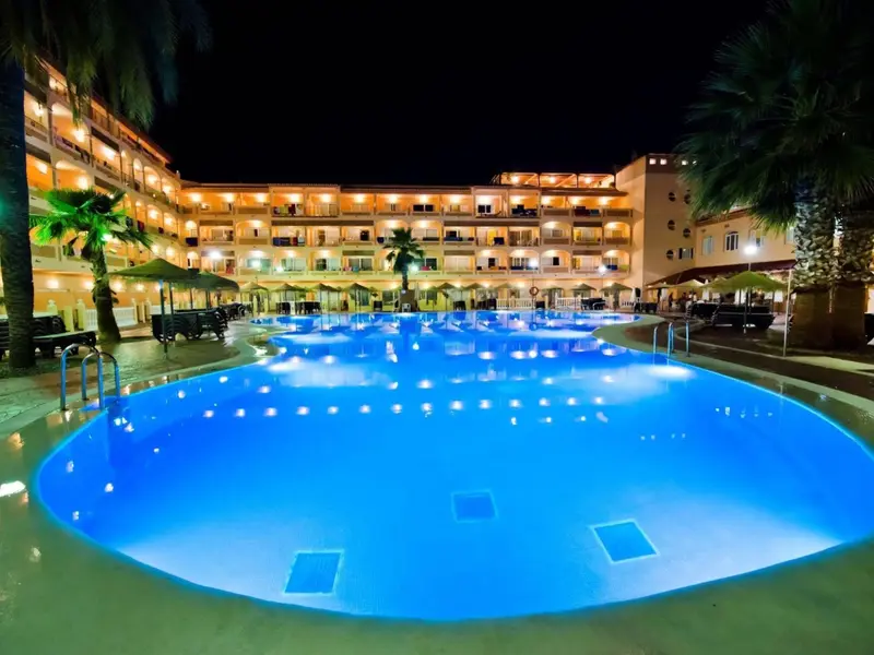 Piscine illuminée devant un bâtiment hôtelier la nuit.