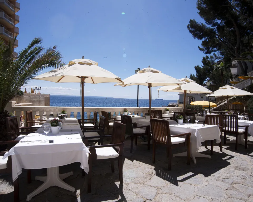 Terrasse ombragée avec tables nappées face à la mer.