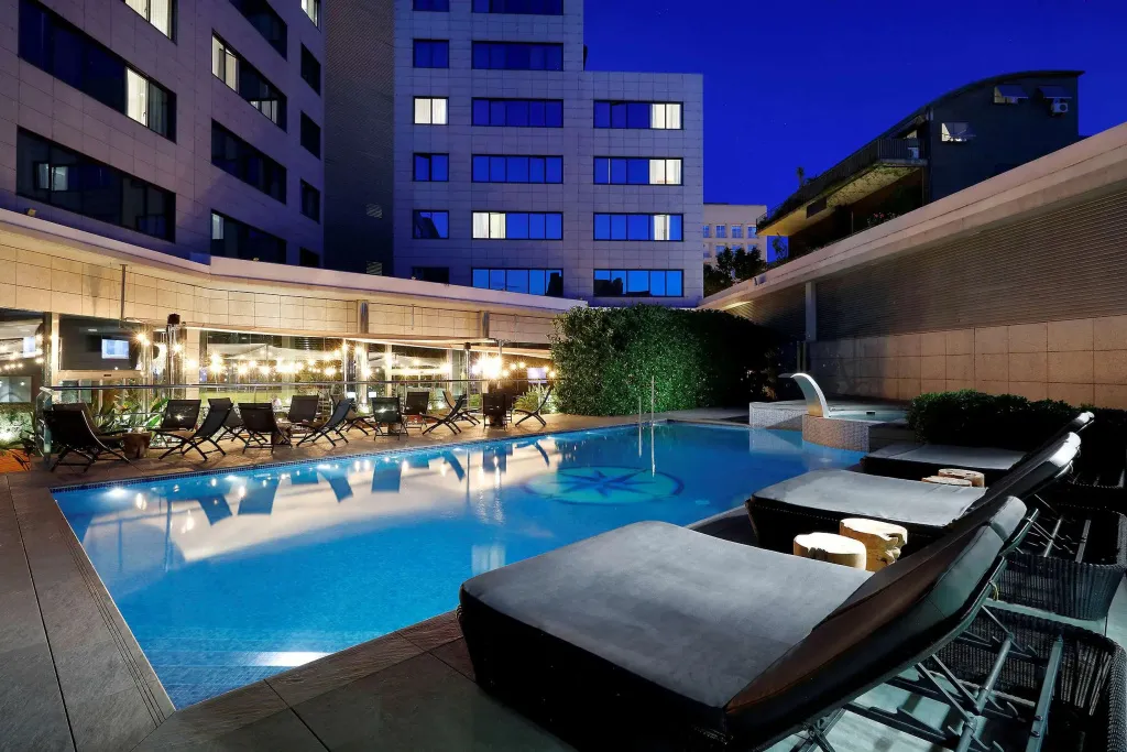 Piscine extérieure avec transats et végétation luxuriante au crépuscule.