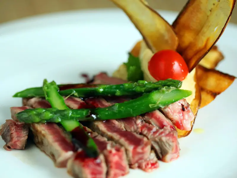Assiette de viande grillée accompagnée d'asperges, d'une tomate cerise et de chips de pommes de terre.