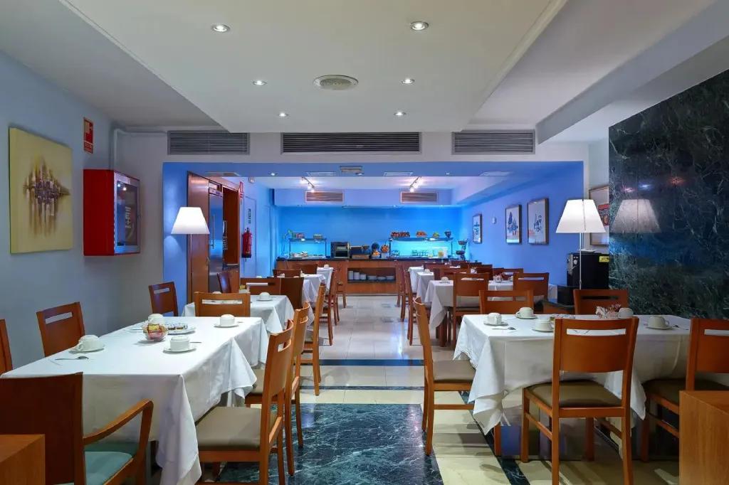 Une salle lumineuse avec des tables dressées pour le petit-déjeuner.