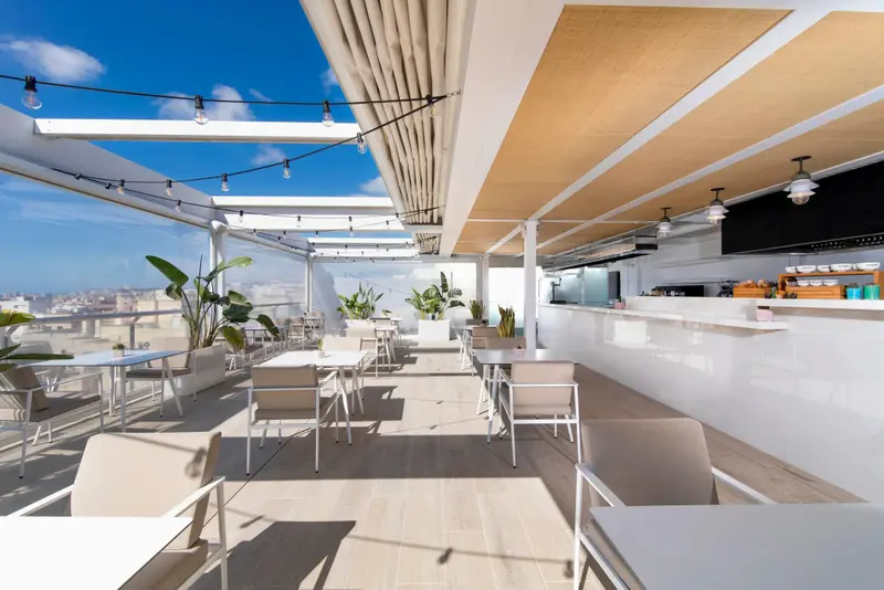 Terrasse aménagée avec tables, chaises et un comptoir de bar ensoleillé.