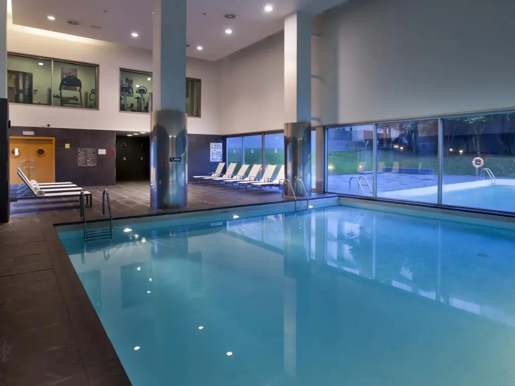 Une piscine intérieure lumineuse avec des transats alignés près de larges baies vitrées.