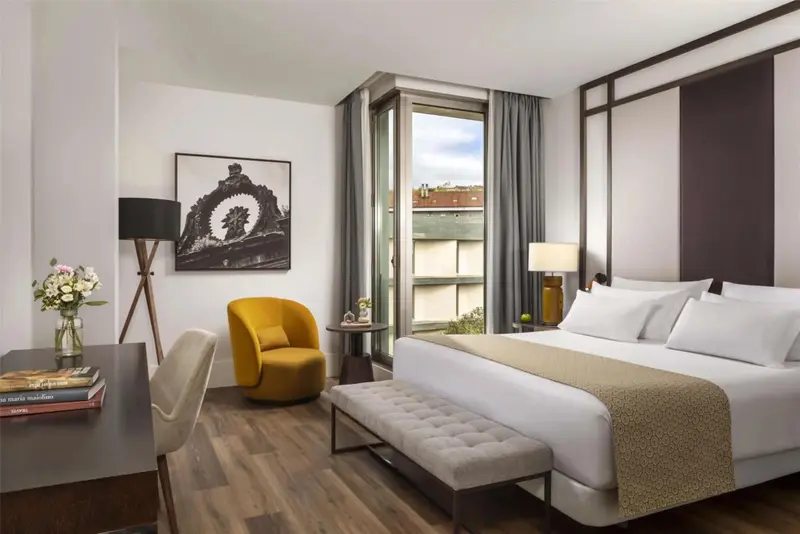 Une chambre lumineuse avec un grand lit et un fauteuil jaune près d'une fenêtre.