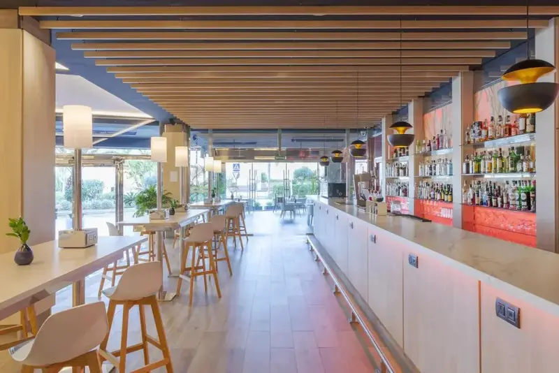 Un long comptoir de bar blanc est bordé de tabourets hauts dans une salle lumineuse.