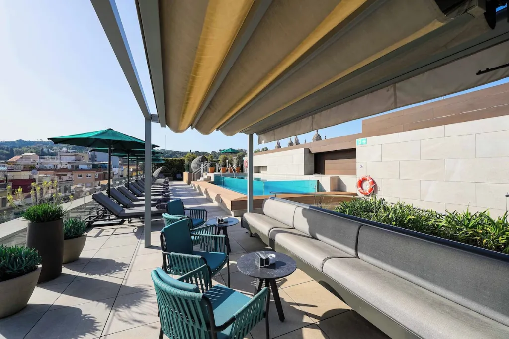 Terrasse aménagée avec des salons et des transats, surplombant une piscine et un paysage urbain.