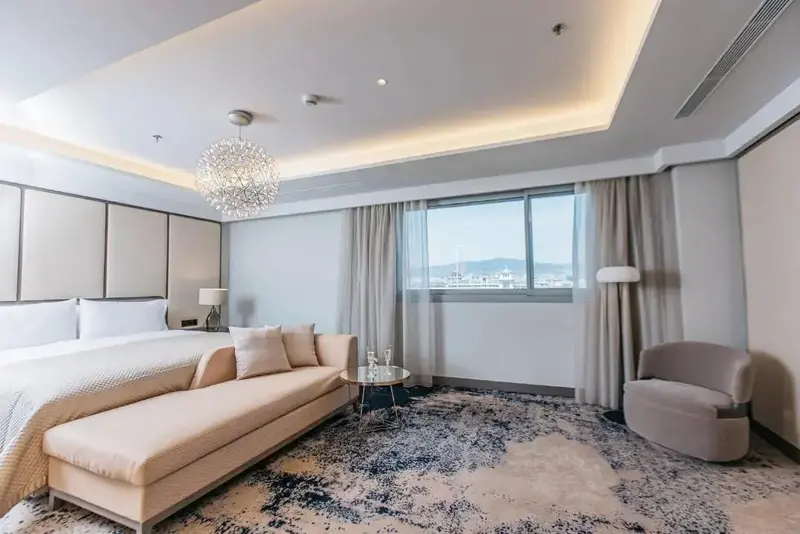 Une chambre lumineuse avec un lit, un canapé et un fauteuil près d'une fenêtre.
