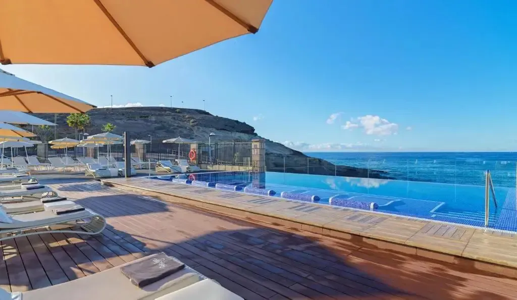Terrasse avec transats et piscine à débordement donnant sur la mer.