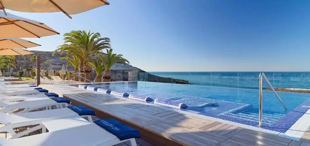 Transats blancs alignés au bord d'une piscine à débordement avec vue sur la mer.