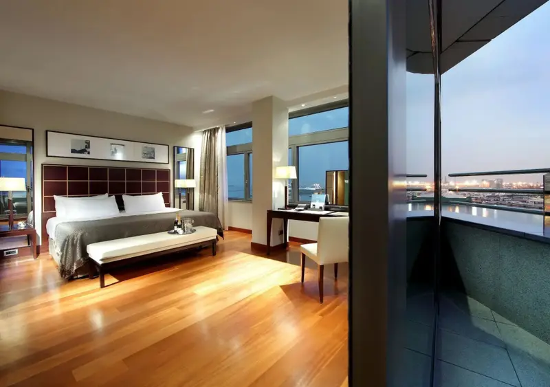 Une chambre spacieuse avec un grand lit et un bureau donnant sur une vue urbaine.