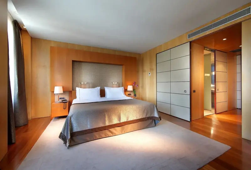 Une chambre lumineuse avec un grand lit et un parquet clair.