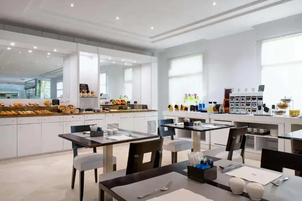 Une salle lumineuse présente des tables dressées pour le petit-déjeuner avec un buffet garni.