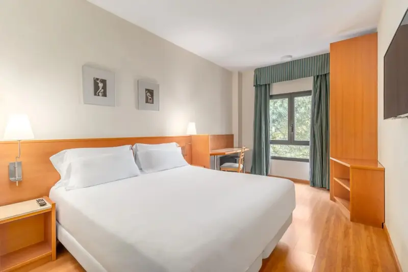 Une chambre lumineuse avec un grand lit et un bureau près de la fenêtre.