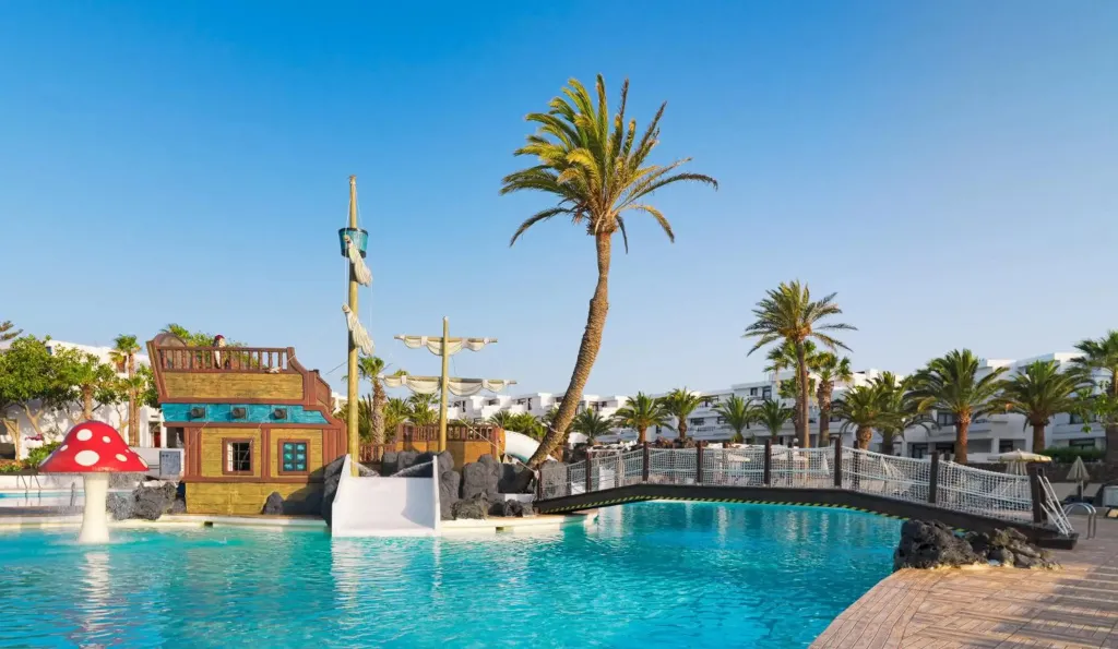 Une piscine avec une structure de jeu sur le thème des pirates et des palmiers.