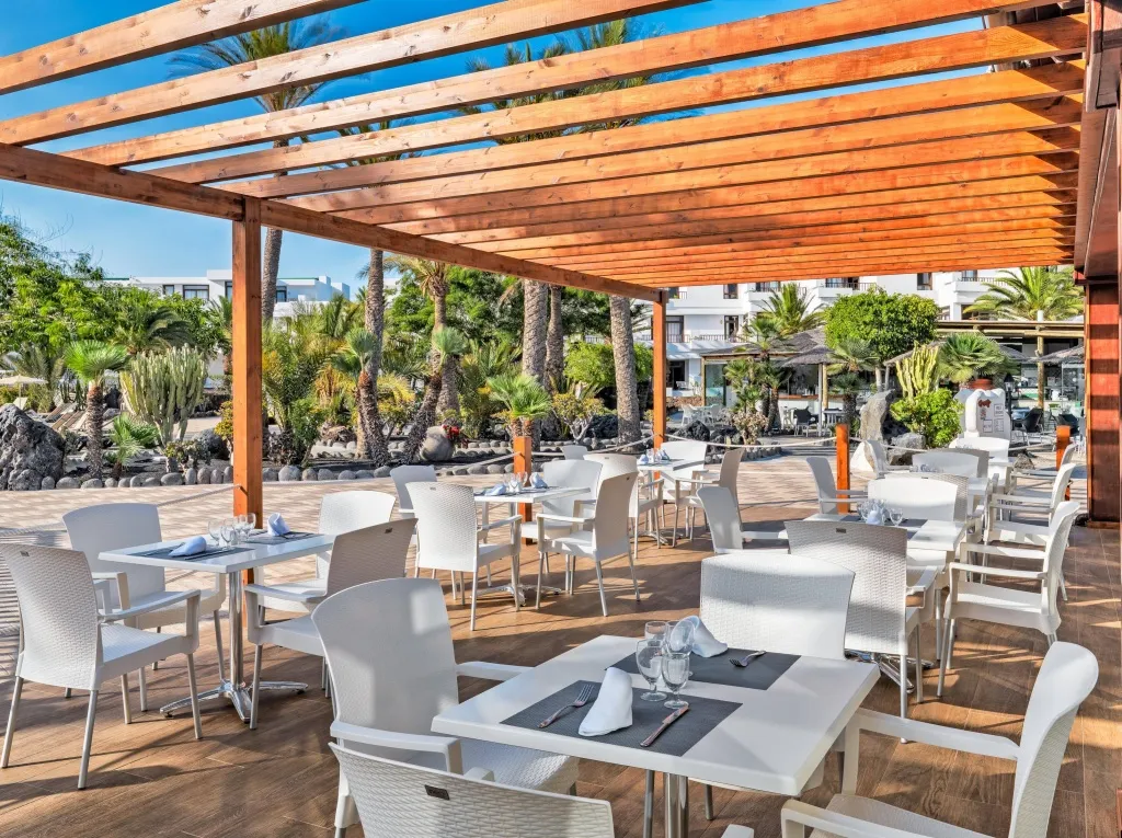 Terrasse ombragée avec tables et chaises blanches prêtes pour le service.