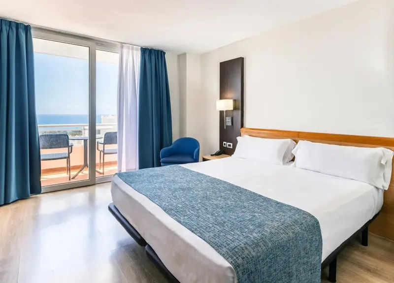 Une chambre lumineuse avec un grand lit donnant sur une terrasse et la mer.