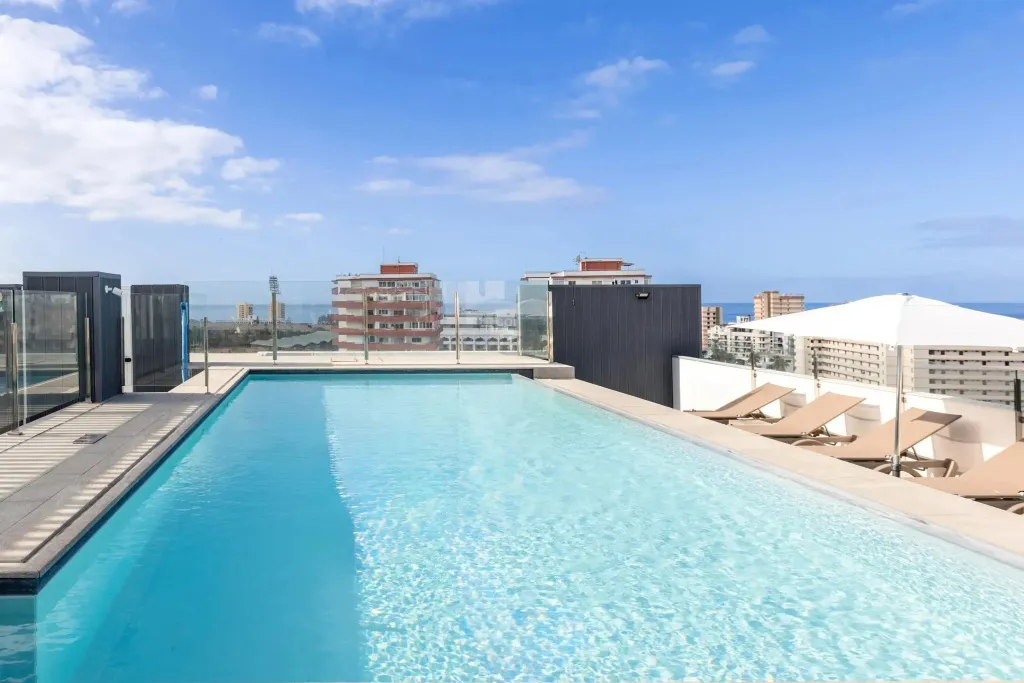 Piscine rectangulaire sur un toit-terrasse avec transats et vue sur la ville et la mer.