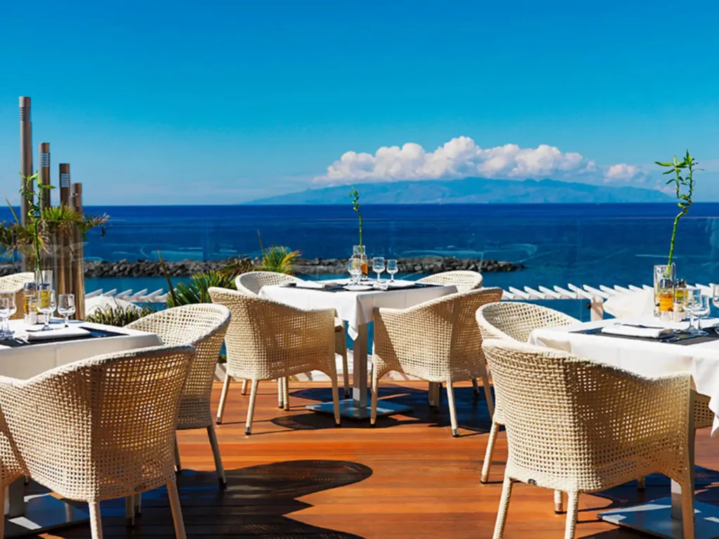 Tables dressées en terrasse avec vue sur l'océan et les montagnes.