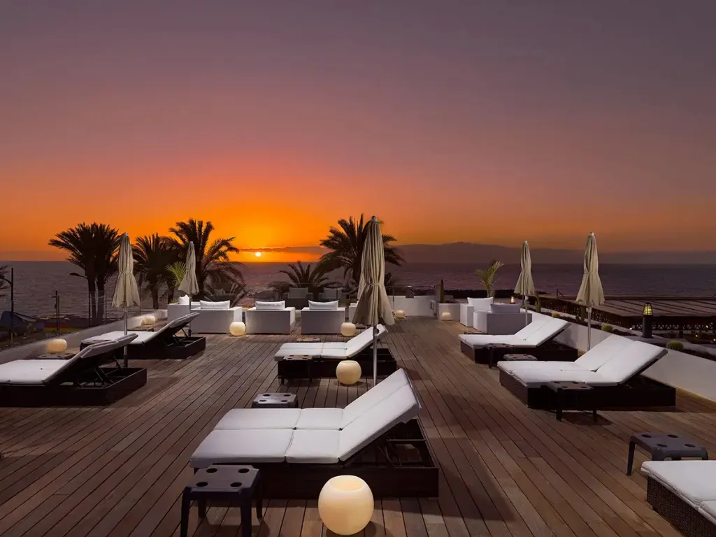 Terrasse aménagée avec des transats face à la mer au coucher du soleil.