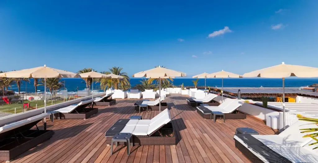 Terrasse en bois avec transats et parasols face à la mer.