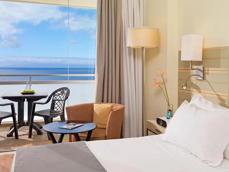 Une chambre lumineuse avec vue sur la mer depuis une grande fenêtre.