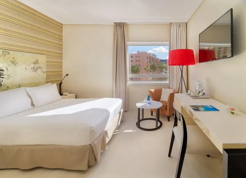 Une chambre lumineuse avec un lit double et un bureau près d'une fenêtre.