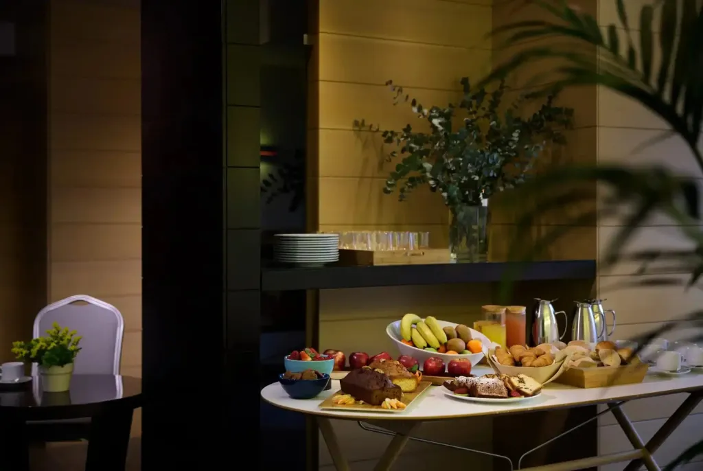 Une table garnie de fruits, viennoiseries et boissons est présentée dans un espace lumineux.