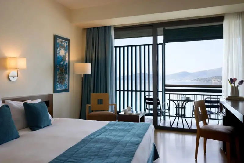 Une chambre lumineuse avec un lit fait et une vue sur la mer depuis un balcon.