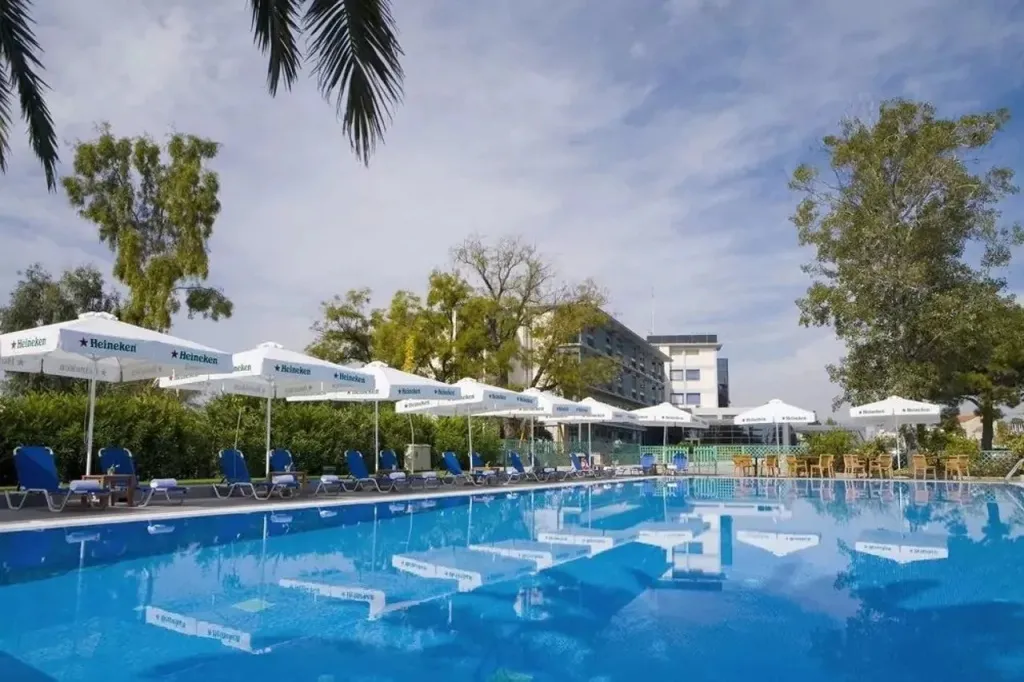 Une piscine bordée de transats blancs sous des parasols, avec un bâtiment en arrière-plan.