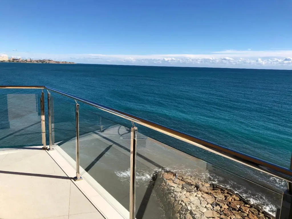 Vue sur la mer depuis une terrasse avec garde-corps en verre.