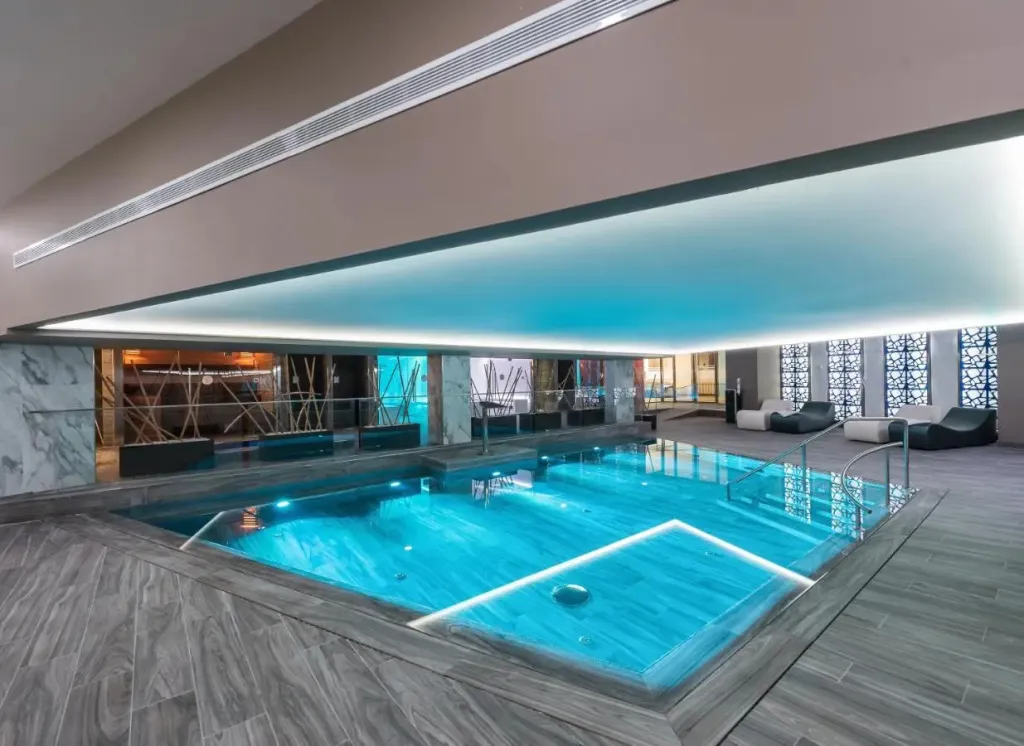 Piscine intérieure lumineuse avec transats et éclairage bleuté.