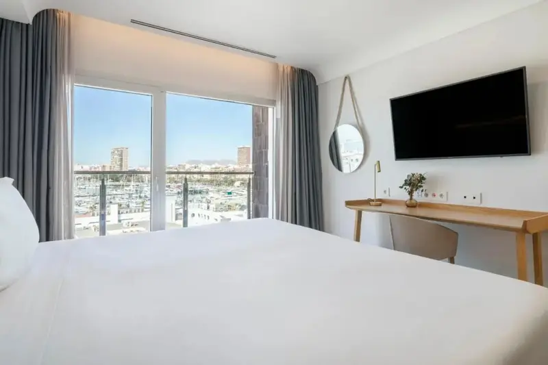 Une chambre lumineuse avec un grand lit et une vue sur le port.