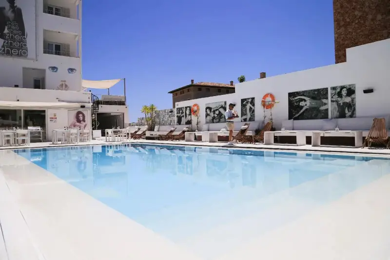 Une piscine rectangulaire bordée de transats blancs sous un ciel bleu dégagé.