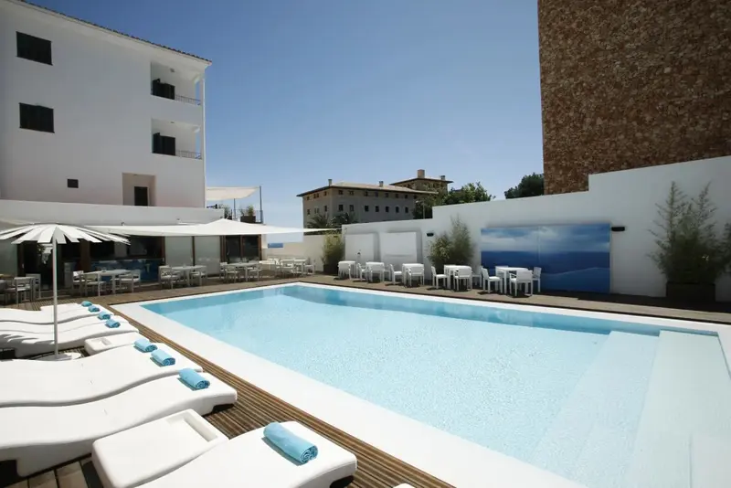 Une piscine rectangulaire bordée de chaises longues blanches sous le soleil.