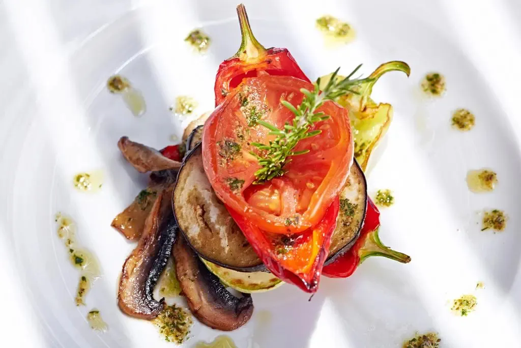 Assiette de légumes grillés décorée d'herbes fraîches et d'un filet d'huile d'olive.