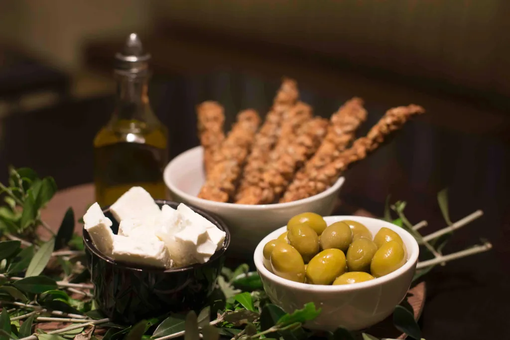 Assortiment d'olives, de fromage et de gressins sur une table sombre.