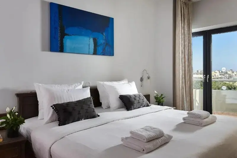 Une chambre lumineuse avec un grand lit recouvert de linge blanc et des coussins décoratifs.