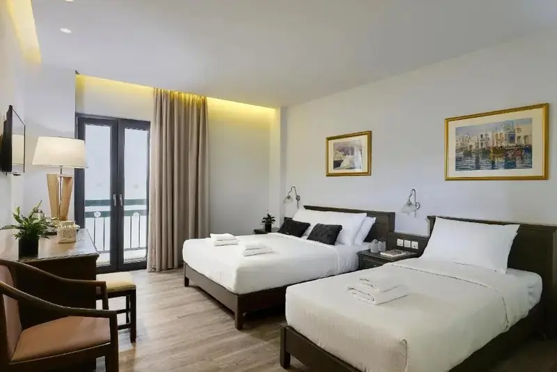 Une chambre lumineuse avec deux lits et un bureau près d'une baie vitrée.