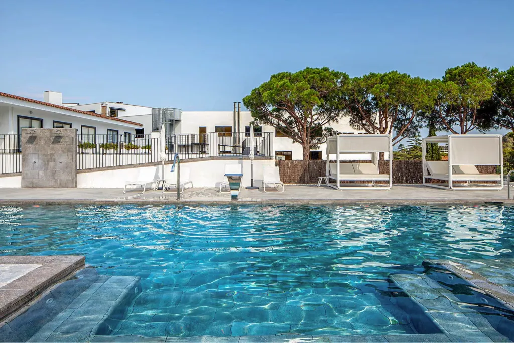 Une piscine bleue avec des transats et des bâtiments blancs en arrière-plan.