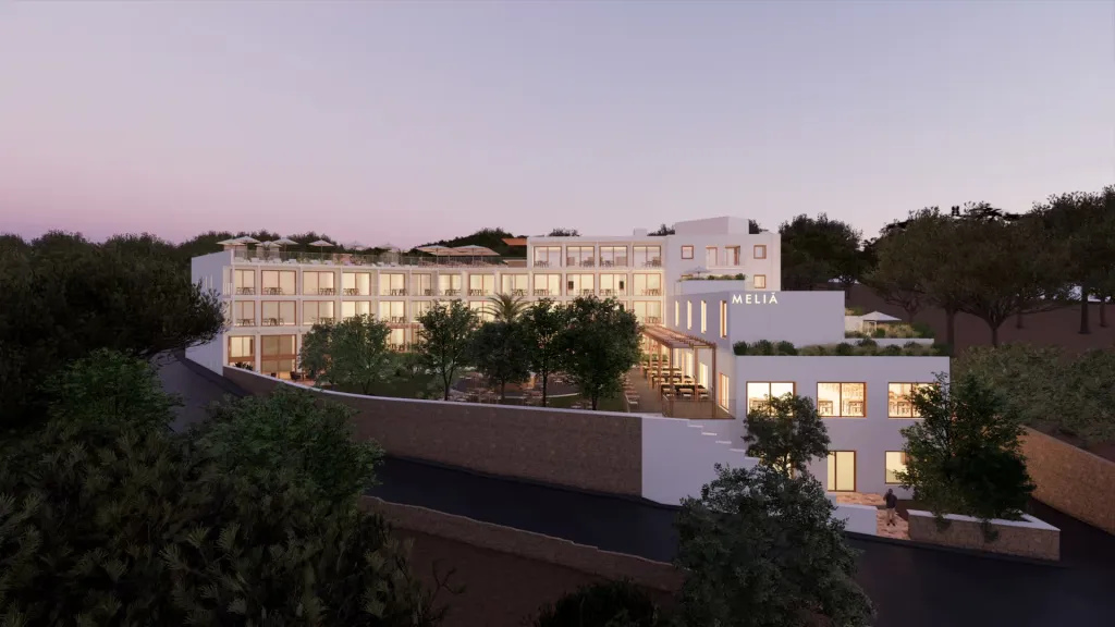 Bâtiment blanc moderne avec des fenêtres et des balcons, entouré de végétation et illuminé au crépuscule.