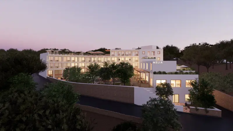 Bâtiment blanc moderne avec des fenêtres et des balcons, entouré de végétation et illuminé au crépuscule.