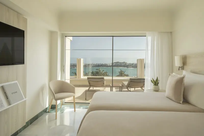 Une chambre lumineuse avec un grand balcon donnant sur la mer.