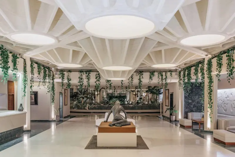 Vaste hall d'accueil lumineux avec une statue centrale et une végétation luxuriante.