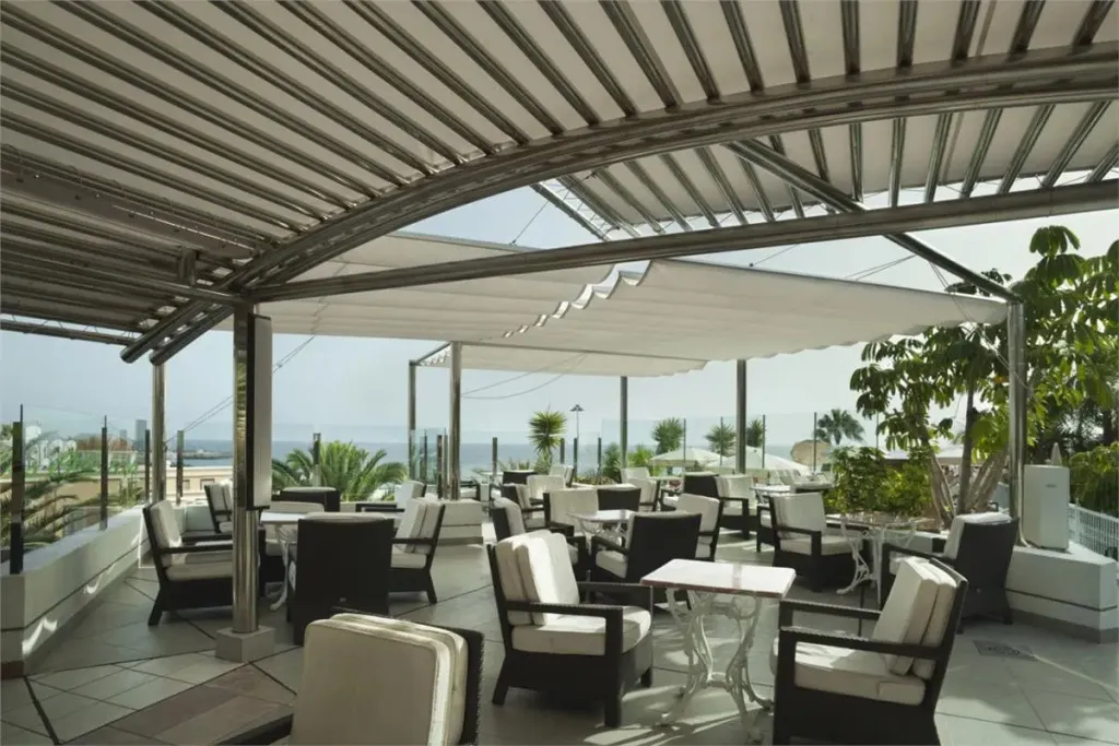 Terrasse ombragée avec mobilier de jardin et vue sur la mer.