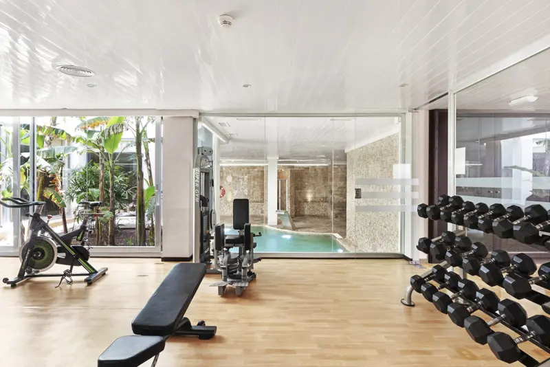 Une salle de sport lumineuse avec des équipements de musculation et une vue sur une piscine intérieure.